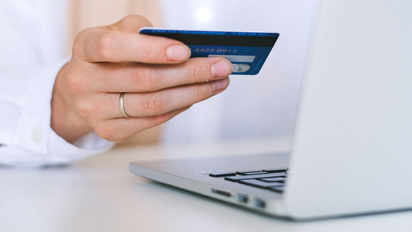 En hand håller ett kreditkort bredvid en laptop